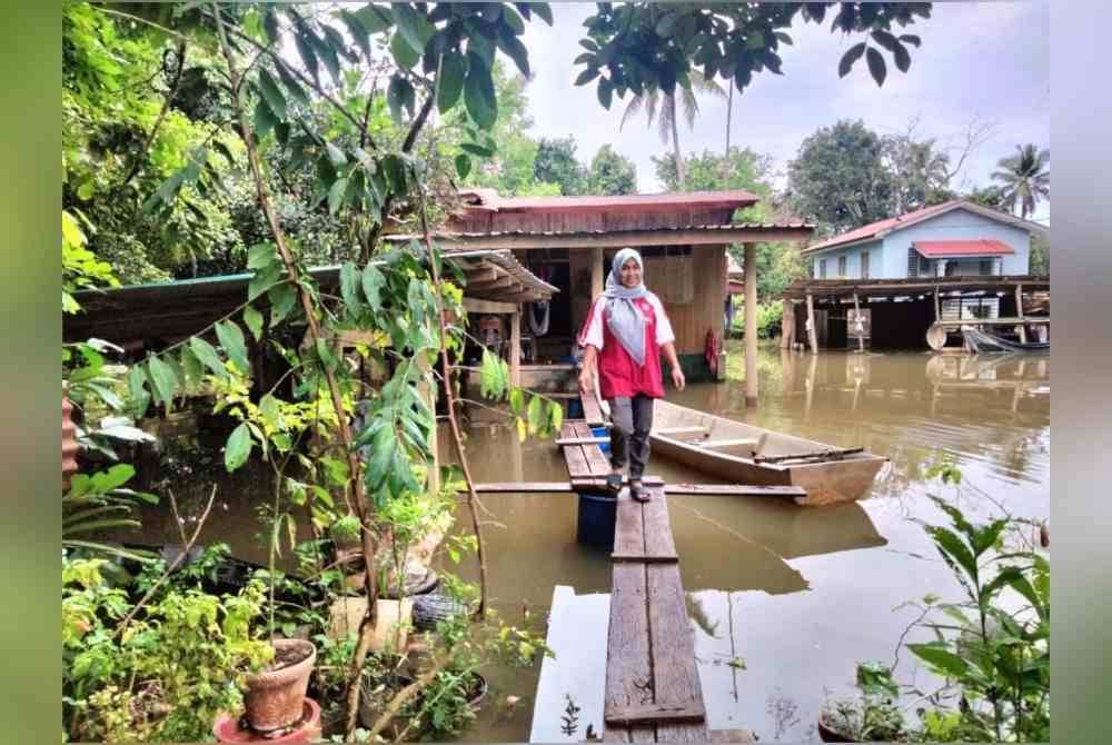 Aifa Shafika menggunakan titi untuk menyeberangi banjir di kawasan rumahnya.