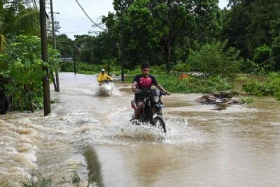 Penduduk meredah banjir pada sebatang jalan yang dilimpahi air ekoran hujan lebat ketika tinjauan di Kampung Buluh. Foto Bernama