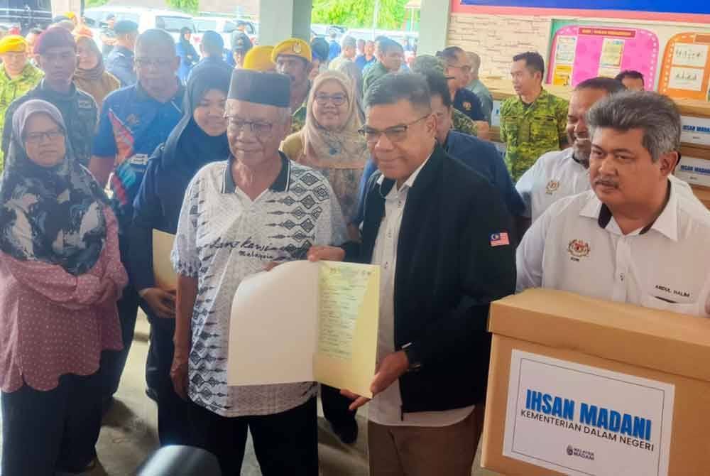 Saifuddin Nasution (dua kanan) menyampaikan dokumen sijil kelahiran yang diperbaharui oleh JPN kepada mangsa banjir di PPS SK Bukit Tinggi, Jitra pada Rabu.