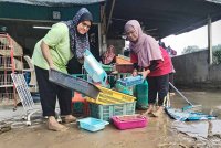 Azmah (kiri) melakukan kerja membersihkan bahagian kedai yang terjejas banjir di Kampung La, Besut