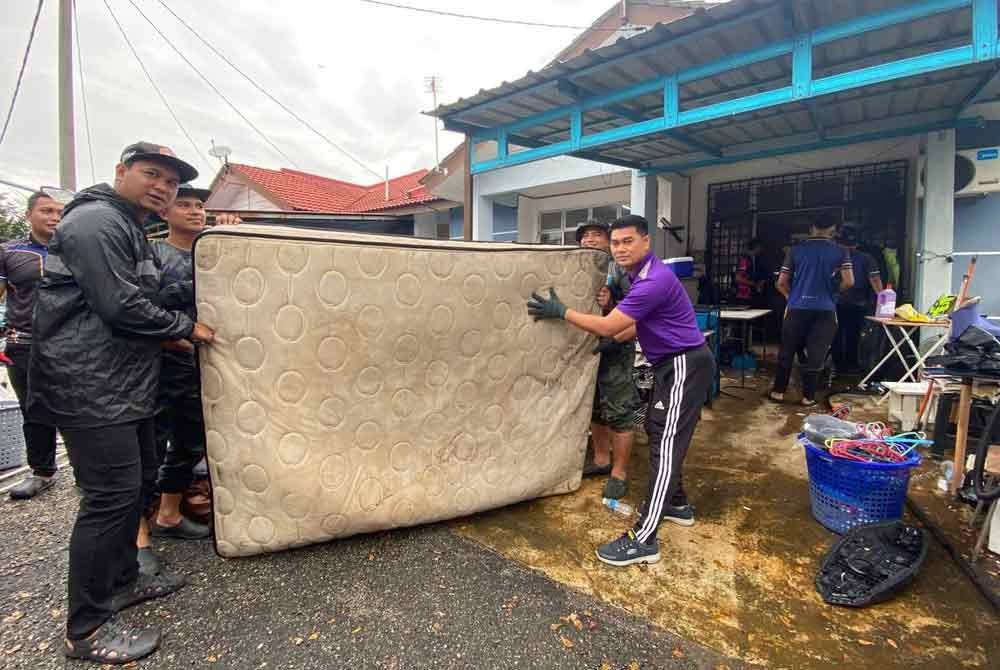 Rizalman (kiri) dibantu pegawai dan anggota polis yang lain membersihkan barangan yang musnah akibat banjir di Taman Sri Bayu, Tumpat pada Isnin.