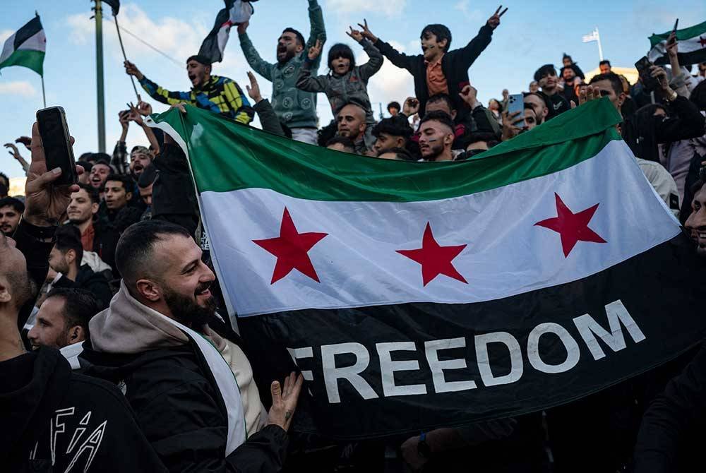 Penduduk memegang bendera Syria di dataran Syntaqma di Athens bagi meraikan kejatuhan rejim Bashar al-Assad. - AFP