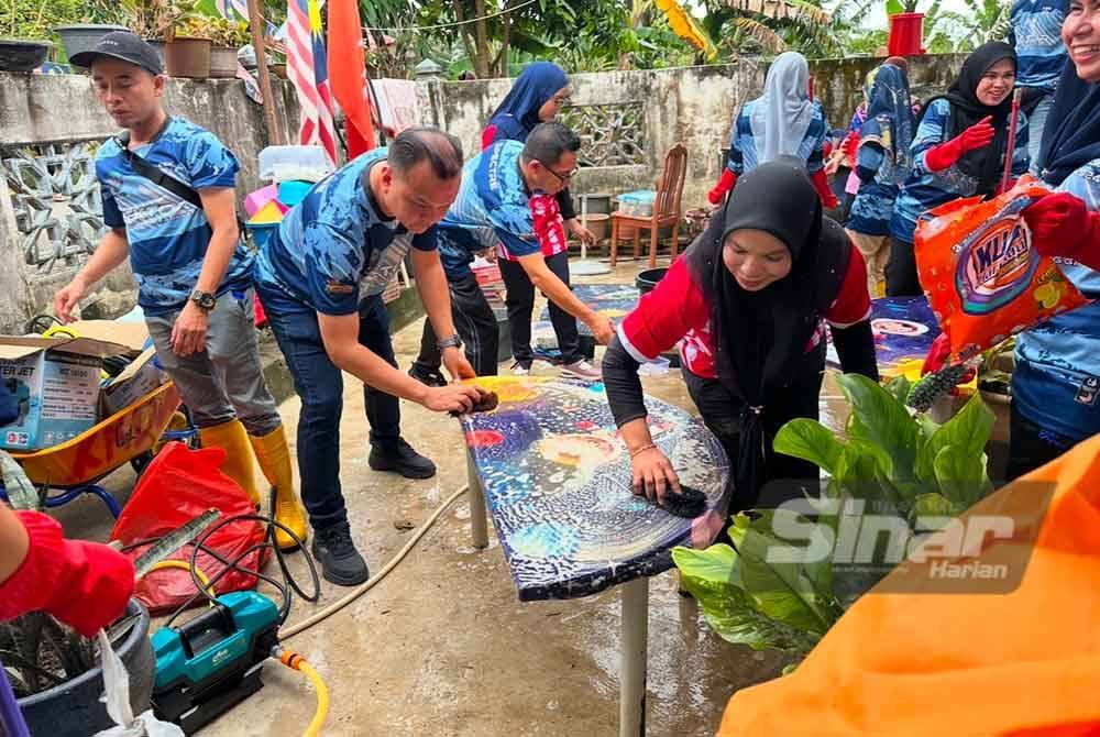 Nasrul Haqiim (dua dari kanan) turut serta mencuci meja yang ditenggelami banjir. FOTO SINAR HARIAN-ADILA SHARINNI WAHID.