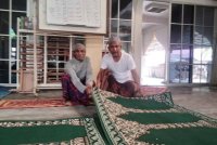 Anuar (kanan) memasang karpet sebelum solat Jumaat.