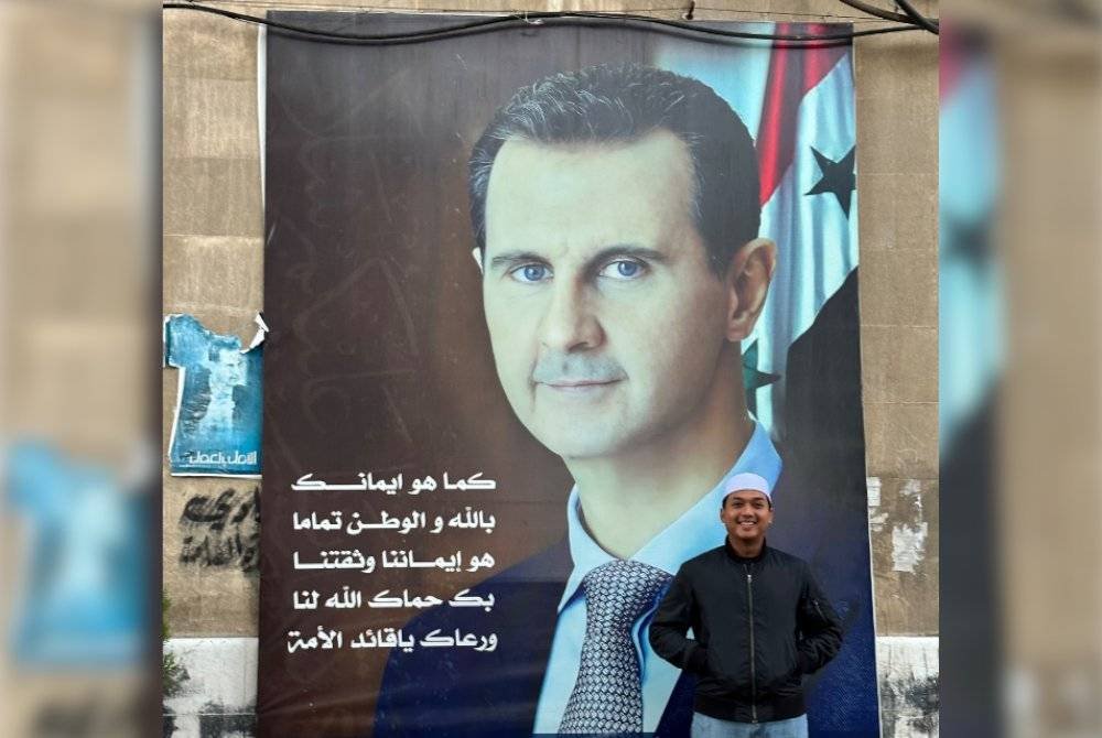 USTAZ MUHAMMAD HASBULLAH bergambar di hadapan poster Presiden Syria, Bashar Al-Assad di Damsyik pada Mac 2023. 