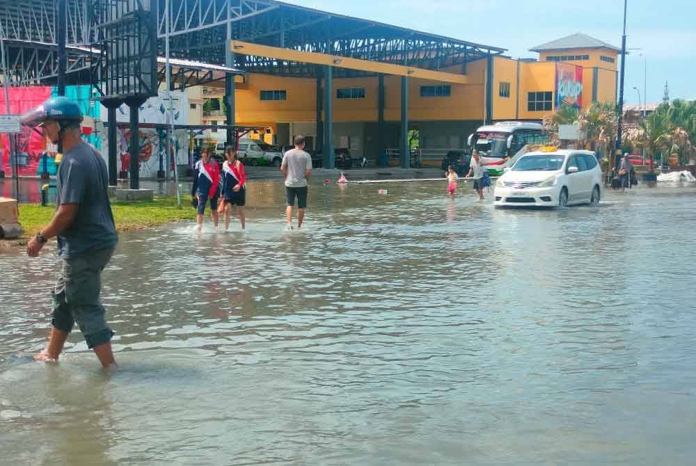 Penduduk berjalan kaki meredah laluan yang dinaiki air akibat kejadian air pasang besar pada pagi Selasa.