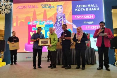 Mohd Azizul Arif (kiri) menyampaikan cenderamata kepada Kamarudin selepas merasmikan MYES -Midnight Sale AEON Mall Kota Bharu pada Selasa.