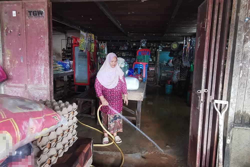 Zaleha membersihkan kedai runcit yang dinaiki air ketika banjir kembali melanda kawasan itu pada Ahad lalu.