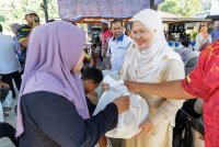 Salbiah (kanan) menyampaikan bantuan sempena Program Penyerahan Bakul Makanan SKM Prihatin, Skuad Ihsan Madani di Dewan Orang Ramai Kampung Plang di sini pada Jumaat.