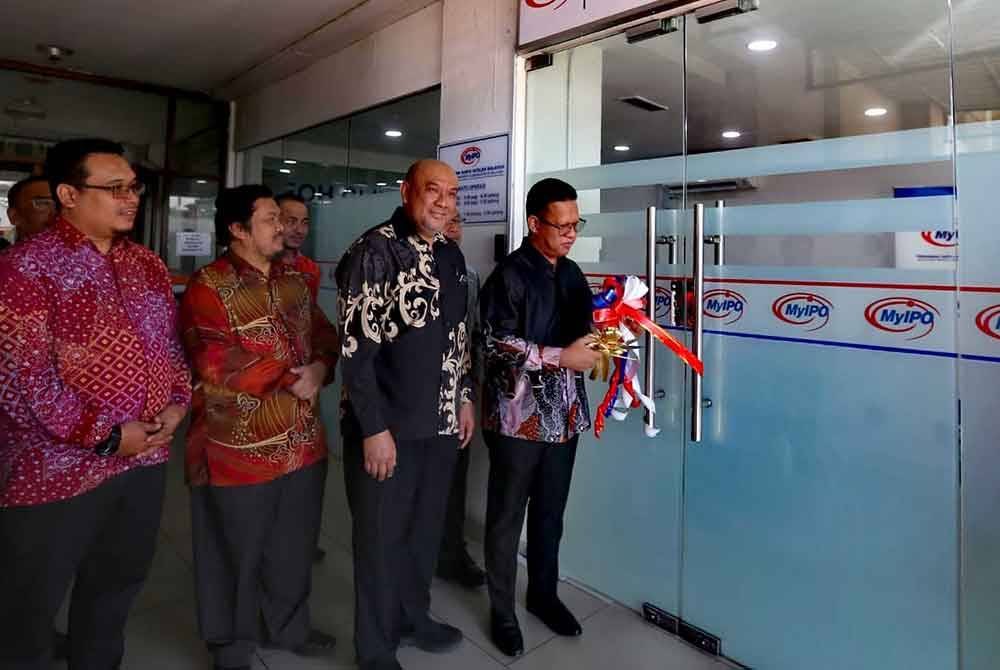 Mohd Zuhan (kanan) memotong riben pada pintu pejabat satelit MyIPO di UTC Alor Setar sebagai simbolik perasmian.