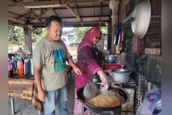 Zahari membantu isteri menggoreng ayam yang dijual di hadapan rumahnya.